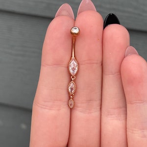 Puede incluir: Anillo de ombligo de oro rosa con tres piedras transparentes de forma marquesa.