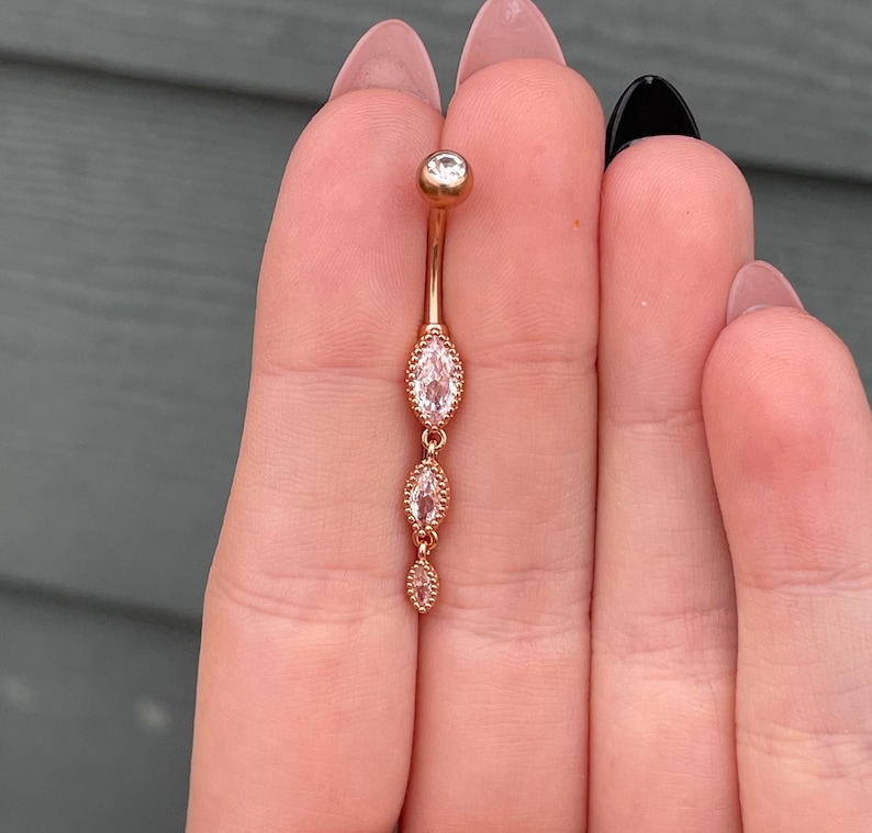 Puede incluir: Anillo de ombligo de oro rosa con tres piedras transparentes de forma marquesa.
