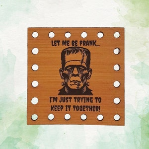 May include: A wooden square sign with a black and white illustration of Frankenstein's monster. The sign reads "Let me be Frank... I'm just trying to keep it together!" and has a border of small holes around the edges.