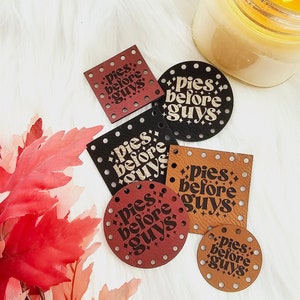May include: Five leather patches with the text "pies before guys" in a retro font. The patches are in various shapes and sizes, including circles and squares. The patches are brown, black, and red.