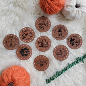 May include: Nine brown leather round patches with black text and designs. The patches have holes around the edges. The patches feature Halloween-themed text and images, including "The Wicked Witch Club", "Baddest Witch Around", "Bad Witch Club", "World Full of Princesses Be A Witch", "Halloween Potion", "Salem Witches Brew Sanderson Sisters Brewing Co", "The Sanderson Sisters Black Flame Candle Company", and "Sanderson".