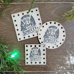 May include: Three wooden ornaments with a Christmas tree design and the text "I like them real thick and spruce" printed on them.