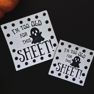 May include: Halloween-themed image with two white square signs that read "I'M TOO OLD FOR THIS SHEET!" with a ghost graphic. The image also features two orange pumpkins and a larger pumpkin with a black spider decoration.