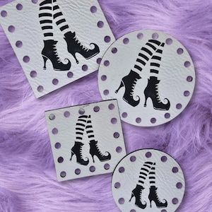 May include: Four white coasters with a black and white striped witch leg design. The coasters are in square and circular shapes, with a series of small holes around the edges. The background is a fuzzy, lavender surface.