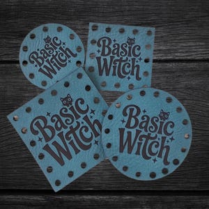May include: Four blue leather-like patches in square and circular shapes, each featuring the dark text Basic Witch, a small cat icon, and star accents. The patches have pre-punched holes along their edges for sewing or attachment purposes.