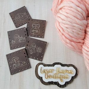 May include: Five brown leather squares with white outlines of sloths in various poses. The sloths are holding drinks, surfing, building sandcastles, and relaxing under an umbrella. The squares are on a light wood surface with a pink yarn ball and a wooden sign that says "Laser Llama Boutique".