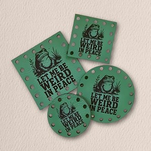 May include: Four green leather-like patches in square and circular shapes, each featuring a black graphic of a frog and the text "LET ME BE WEIRD IN PEACE." The patches have pre-punched holes along their edges for sewing or attachment purposes.