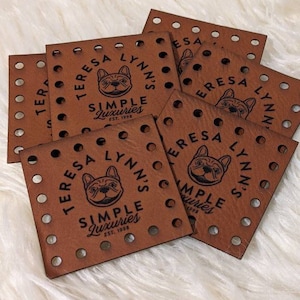 May include: Several brown leather squares with holes punched in them. Each square features a black logo with a dog silhouette and the text "TERESA LYNN'S SIMPLE Luxuries EST. 1998".