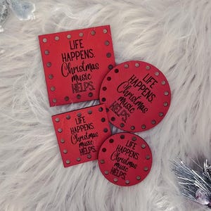 May include: Red Christmas-themed decorations with the text "LIFE HAPPENS. Christmas music HELPS" in a variety of shapes. The decorations are surrounded by white faux fur, a pine cone, and frosted greenery.