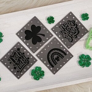 May include: Four gray square patches with different designs, including a shamrock, a rainbow, the words "No Luck Given", and the words "Deo Lucky". The patches are surrounded by green glitter shamrocks and the words "laser llama boutique" in green.