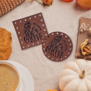 May include: Brown leather coasters with a humorous design. The coasters feature a skeleton illustration holding a coffee cup, with the text "I hate everyone but coffee helps." One coaster is square, the other round.