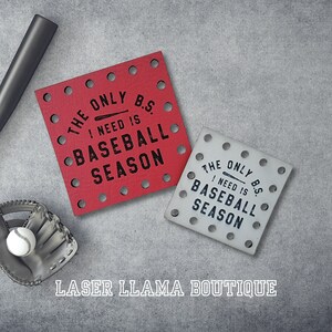 Peut inclure: Deux sous-verres rouges et blancs avec le texte "The only B.S. I need is baseball season". Les sous-verres sont en bois et ont un design découpé au laser. Les sous-verres sont sur un fond gris.