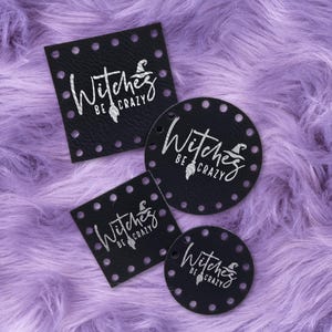 May include: Four black leather tags with the text "Witches Be Crazy" in white script. The tags are in various shapes: square, diamond, and two circles. Each tag has small, evenly spaced holes around the edges. The background is a fuzzy, lavender surface.