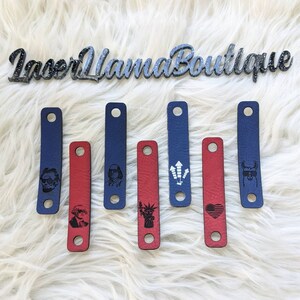 May include: Seven leather straps with different designs, including a portrait of a man wearing sunglasses, a portrait of a man with a hat, fireworks, a heart with stars, a llama wearing sunglasses, and the Statue of Liberty. The straps are in red and blue.