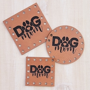 Peut inclure: Trois plaques en bois brun avec le texte "Dog Mom" et une empreinte de patte avec un cœur au centre. Les plaques sont de formes et de tailles différentes, avec un carré, un rond et un petit carré.