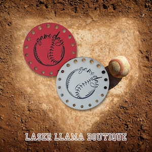 Peut inclure: Deux sous-verres ronds en feutre pour le jour du match avec un motif de baseball et le texte "game day". Un sous-verre est rouge et l'autre est gris. Un ballon de baseball est posé sur le sol à côté des sous-verres.