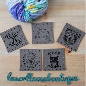 May include: Five gray square fabric patches with black text and designs. The patches feature the following text: "Take it Easy", "The greater the storm, the brighter your rainbow", "Dreamer", "Love her but leave her wild", and "Keep going".