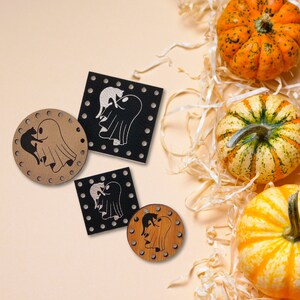May include: Four wooden Halloween decorations featuring a ghost and a cat. The decorations are in different shapes and sizes, with some having a black background and others a brown background. The decorations are on a light brown background with some shredded paper and pumpkins.
