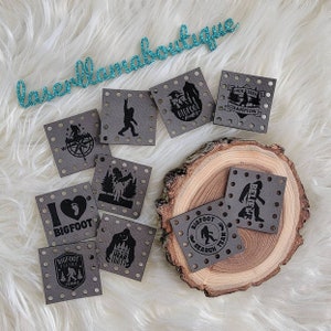 May include: Eight grey square patches with black text and images. The patches feature Bigfoot-themed designs, including "I love Bigfoot", "Bigfoot Search Team", "Believe", "Hide and Seek Champion", and "Bigfoot Hunter".