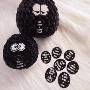 May include: Two black fuzzy ornaments with white googly eyes and various black and white circular tags with text. The tags include phrases like "Can Naughty also mean NICE?!", "100% Pure Imported Coal", "Black like your soul", "Avoid the pressure. Stay Coal", "Santa, can you check a THIRD time?!", "I shine under pressure", and "Just a little lump o' coal".