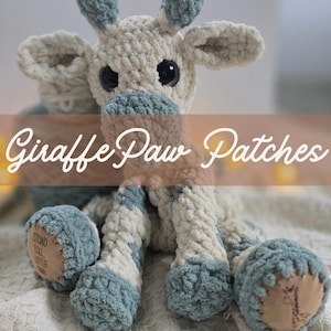 May include: A handmade crochet giraffe plush toy in cream and blue. The giraffe has large black eyes, blue accents, and the text "Giraffe Paw Patches" across the image. The plush has a soft, textured appearance and a small patch on its foot.