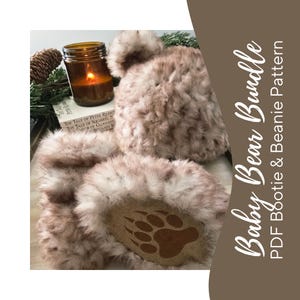 May include: A baby bear bundle featuring a beanie and booties. The booties have a brown paw print design on the soles. The set is a light brown color with a fluffy texture. The image also includes a candle and a book.