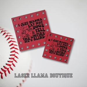 Peut inclure: Deux sous-verres en cuir rouge avec un graphique de joueur de baseball noir et le texte "I just wanna eat hot dogs & tell the umpire he's blind". Les sous-verres sont décorés de petits trous autour des bords. Le texte "LASER LLAMA BOUTIQUE" est imprimé en noir sous les sous-verres.