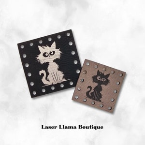 May include: Two leather patches featuring cat designs. The patch on the left is black with a white cat, and the patch on the right is brown with a black cat. Both patches have a circle pattern around the edges.