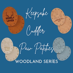 May include: Set of three brown and blue leather patches featuring woodland animal designs. The patches are round and have a stitched border. The text on the patches reads "Deerly Loved", "Moose on the Loose", and "Unbearably Cute". The text "Keepsake Cuddler Paw Patches Woodland Series" is written in white on a blue background.