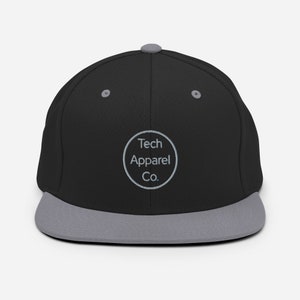 Può includere: Cappellino da baseball nero e grigio con un logo circolare bianco che dice "Tech Apparel Co."