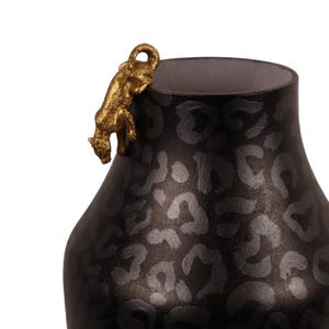 Può includere: Vaso nero con motivo leopardato e una statuetta dorata di leopardo che si arrampica sul bordo. Il vaso ha una base larga e un collo più stretto, con un interno neutro.