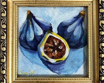 May include: Oil painting of figs in a gold frame. The artwork features three dark blue figs, one sliced open to reveal the interior. The background is light blue, and the frame has ornate detailing.