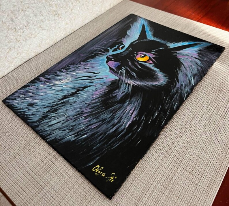May include: A black cat with yellow eyes is painted on a black canvas. The cat's fur is painted with shades of blue and purple. The artist's signature, "Olivia-Ji", is in the bottom right corner of the painting.