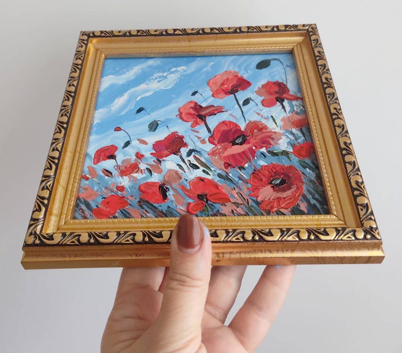 May include: A framed painting depicting a field of red poppies against a blue sky. The painting is in a gold frame with an ornate border.