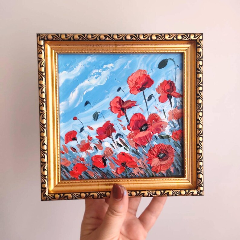 May include: A framed painting depicting a field of red poppies against a blue sky with white clouds. The painting is executed in a loose, impressionistic style.
