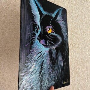 May include: A black cat with bright yellow eyes is painted on a black canvas. The cat's fur is painted with shades of blue and purple, creating a vibrant and colorful effect.