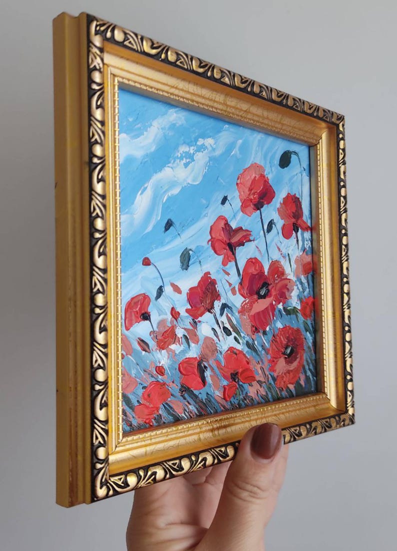 May include: A framed painting depicting a field of red poppies against a blue sky with white clouds. The frame is gold with an ornate design.