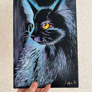 May include: A black cat with yellow eyes is painted on a black canvas. The cat's fur is painted with shades of blue, purple, and white. The artist's signature, "Olga", is in the bottom right corner.