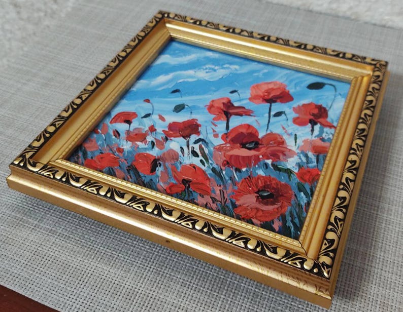 May include: A framed painting depicting a field of red poppies against a blue sky. The frame is gold with a black ornate design.