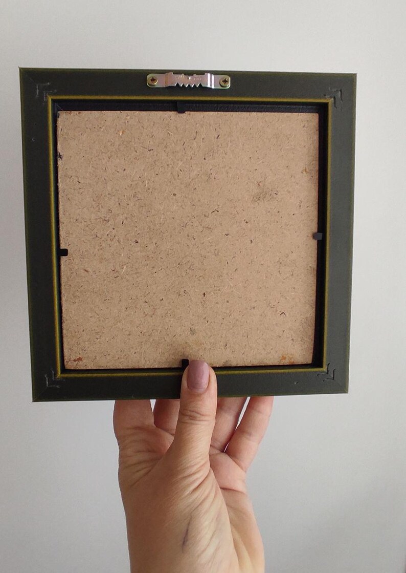 May include: The back of a dark green picture frame with a brown cardboard backing. The frame has a metal hanging hook on the top.