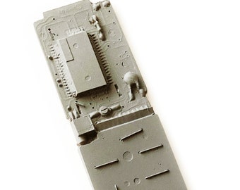 May include: A gray plastic mold with a rectangular shape and a textured surface. The mold has a series of holes and grooves on the bottom.