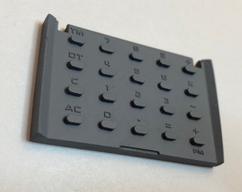 May include: A gray calculator keypad with a variety of buttons, including numbers, operators, and functions. The buttons are labeled with the following text: AC, C, DT, TM, 7, 8, 9, 4, 5, 6, 1, 2, 3, 0, =, +, -, x, and ÷.