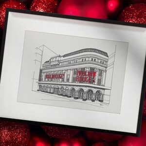 May include: A framed black and white sketch of the Moulin Rouge building, with the words "MOULIN ROUGE!" in red. The artwork is set against a backdrop of red Christmas baubles. The frame has a white mount.