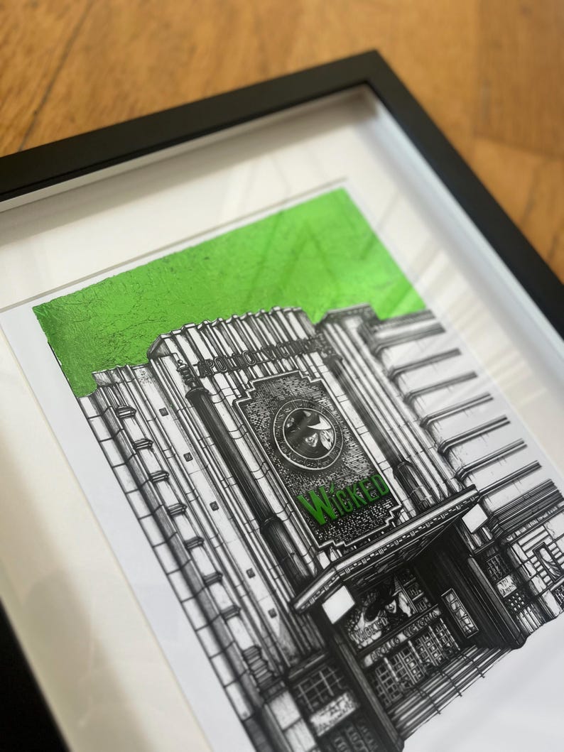 Puede incluir: Un dibujo en blanco y negro del exterior de un teatro con la palabra "Wicked" en letras verdes sobre la entrada. El dibujo est&aacute; enmarcado y tiene un fondo verde.