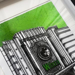 Puede incluir: Una ilustraci&oacute;n en blanco y negro de un edificio de teatro con la palabra "Wicked" en letras verdes en la fachada. El edificio tiene un fondo verde.