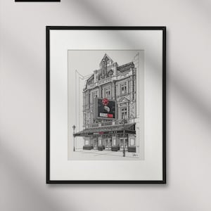 以下が含まれることがあります： 「HADES TOWN」の看板と赤いバラが特徴の劇場のファサードを描いた、白黒の額装アートプリント。アーティストのサインとロゴが左上にあります。