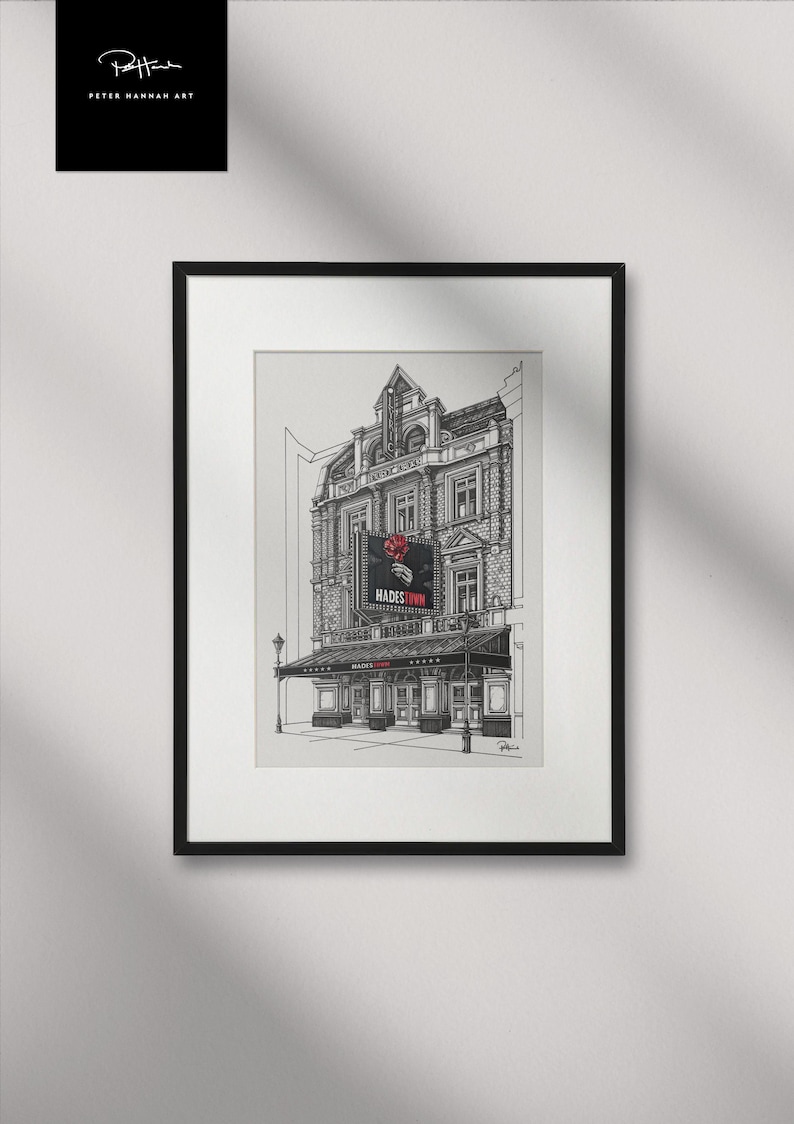 Op de afbeelding: Zwart-wit ingelijste kunstdruk van een theatergevel met een "HADES TOWN"-reclamebord en een rode roos. Handtekening en logo van de kunstenaar staan in de linkerbovenhoek.
