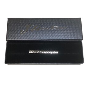 Puede incluir: Un pasador de corbata plateado con un diseño texturizado viene en una caja negra con el nombre de la marca "Zaffiro" impreso en la parte superior.