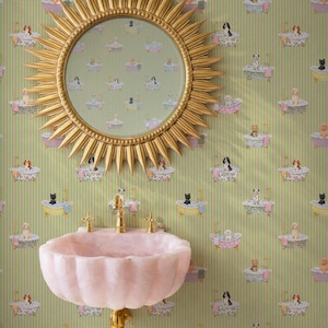 Puede incluir: Una escena de baño caprichosa con un espejo dorado en forma de sol, un lavabo rosa festoneado con grifos dorados y papel pintado con un patrón repetido de perros y gatos en bañeras. El papel pintado tiene un fondo a rayas verdes y blancas.
