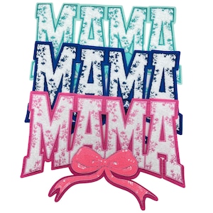 May include: Three felt patches spelling out "MAMA" in different colors. The top patch is light blue with white floral accents, the middle patch is navy blue with white floral accents, and the bottom patch is pink with white floral accents. A pink bow with sequins is attached to the bottom patch.